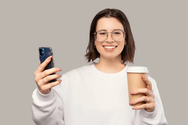 Donna felice è in possesso di un telefono e una tazza di caffè take away fatta di carta. — Foto Stock