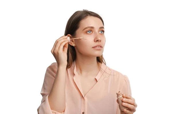 Serious young woman is using a tube of make up foundation or concealer. — 스톡 사진