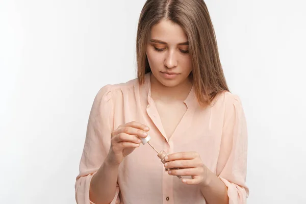 Serious woman is holding a tube of make up foundation while looking at it. — Photo