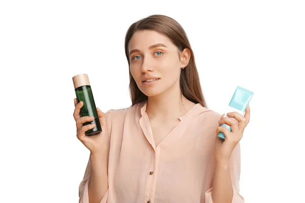 Beautiful woman is holding toner and cream tube while looking at the camera. — 스톡 사진