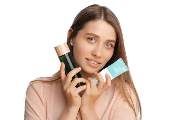 Beautiful young woman is holding toner and cream tube close to her face. — Photo