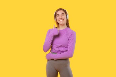 Spor giyim ve kulaklık takan mutlu kadın başparmağını kaldırıyor..