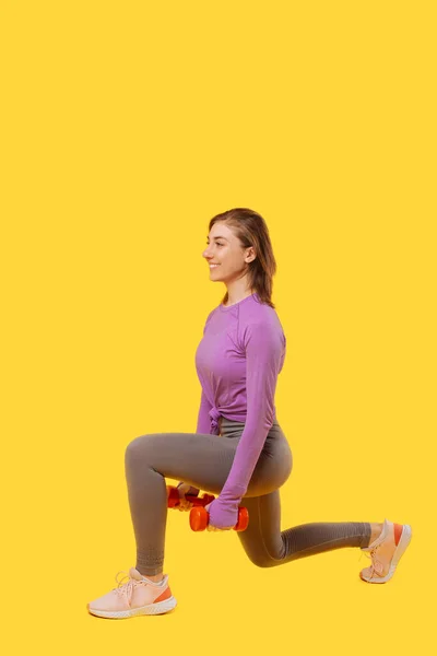 Vertical photo of a young woman performing lunges with dumbbells in a studio. — Fotografia de Stock