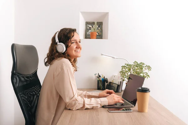 Photo of smiling office woman in casual listening podcast and wireless headphones. — стоковое фото