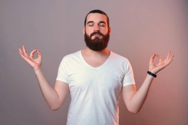 Kapalı gözlü sakallı adam stüdyoda zen jesti yapıyor..