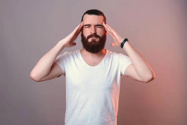 Displeased bearded man is holding hands on his head because of a headache. — Stock Fotó