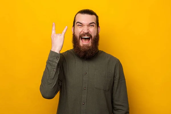 Sikoltozó fiatal szakállas férfi mutatja rock gesztus felett sárga háttér. — Stock Fotó