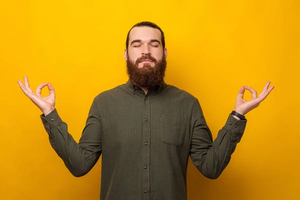 Fiatal szakállas férfi fogja a kezét zen gesztus felett sárga háttér. — Stock Fotó