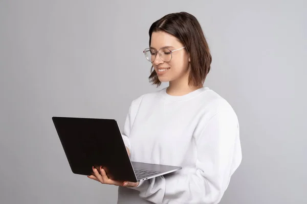 Concentrato donna sorridente con gli occhiali è in possesso di un computer portatile mentre in piedi. — Foto Stock