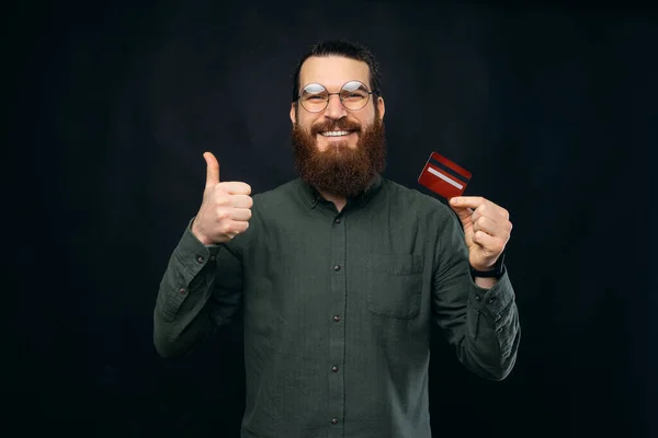 Hey this is a new credit card, happy young hipster man showing thumb up gesture and debit card.