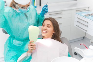 Smiling blonde girl is looking in the mirror checking out her beautiful teeth.