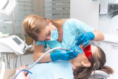 Eldiven giyen kadın dişçi çalışıyor ve genç bir kadının ağzına bakıyor..