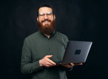 Neşeli sakallı bir adam dizüstü bilgisayarını tutuyor ve gözlükleriyle gülümsüyor kameraya bakıyor.