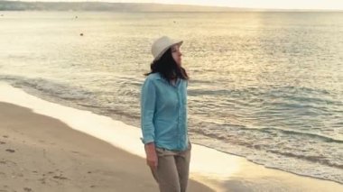 Genç bir kadının gün doğumunda deniz kenarında günlük yürüyüşünün videosu..