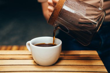 Birilerinin elinde çaydanlık kahvesinden beyaz bir fincana dökülen bir fotoğraf. .