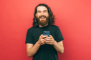 Genç sakallı bir adamın fotoğrafı. Telefonundan biriyle konuşuyor ve kameraya gülümsüyor.