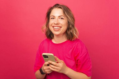 Neşeli genç bir kadın telefonla birine mesaj atıyor ve doğrudan kameraya bakıp gülümsüyor.