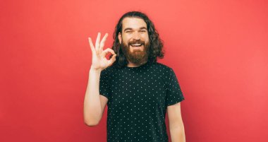 A photo of a young bearded man showing the ok sign and smiling at the camera