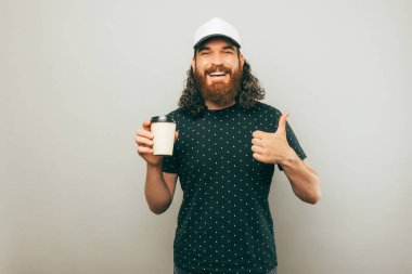 A delivery man is showing a thumg up while holding a cup of coffee and smiling at the camera