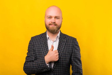 A photo of a young bearded man holding a thumb up while smiling at the camera