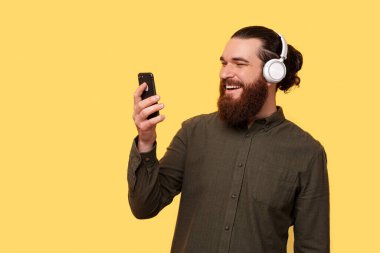 A young bearded man is picking a song from his phone to listen to his new headphones