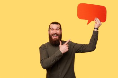 A bearded man cheerfuly pointing at a speech bubble while looking at the camera