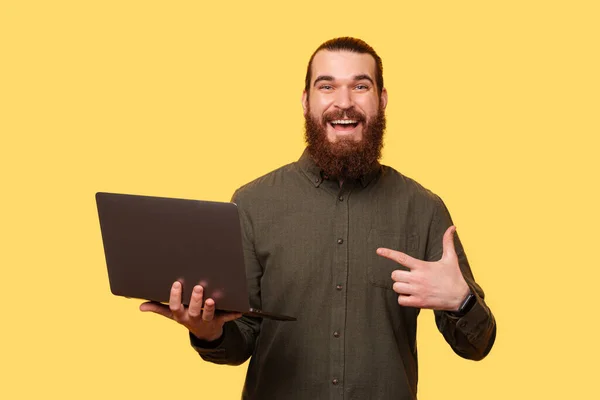 Young Bearded Man Pointing His New Computer While Smiling Camera — Foto de Stock