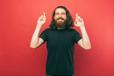 A photo of a young bearded man holding his fingers crossed wishing something