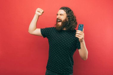 A happy bearded man is being very excited while holding his phone