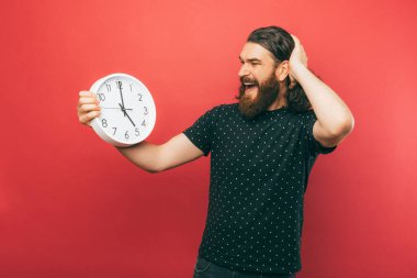 A photo of a an excited bearded man holding a white clock while he is looking at it
