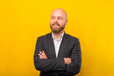 A photo of a young bearded man standing with crossed arms looking away and smiling