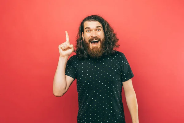 A cheerful bearded man is pointing up at a free space while he is looking excited at the camera