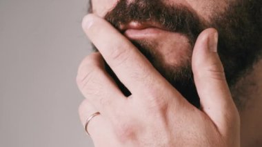 Close up video of man touching his beard and thinking.