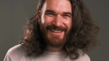 Close up footage of young handsome bearded man with long hair looking at the camera and smiling.