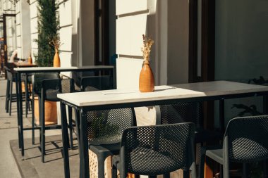 Urban scene of a nice terrace of an european cafe with no people in sunlight. Black and white furniture.