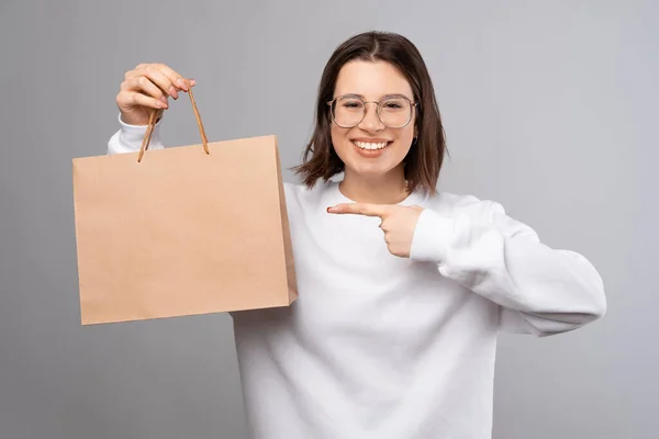 Young Lady Wearing White Sweatshirt Points Shopping Bag She Holding — стоковое фото