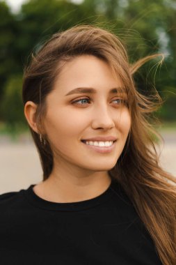 Rüzgarlı bir günde gülümseyen sarışın bir kadının dikey yakın portresi..