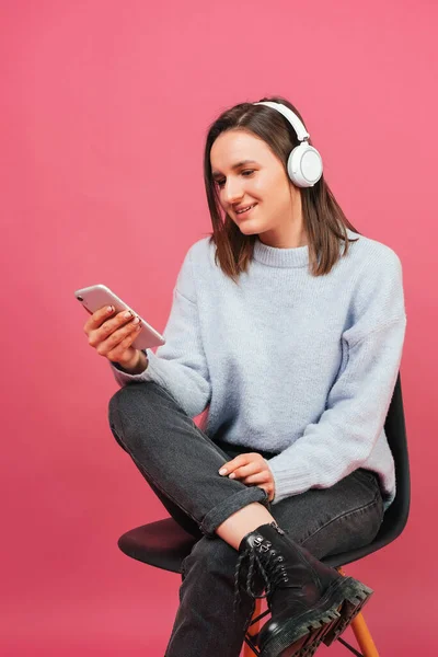 여자는 음악을 둘러보고 헤드폰을 의자에 분홍색 배경으로 촬영된 스튜디오 — 스톡 사진