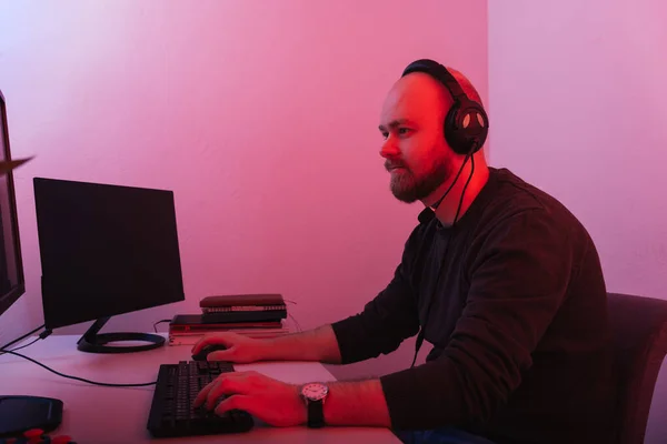 ヘッドセットを身に着けているひげそりの男が座っていて コンピュータで働いています 赤信号で撃たれた — ストック写真