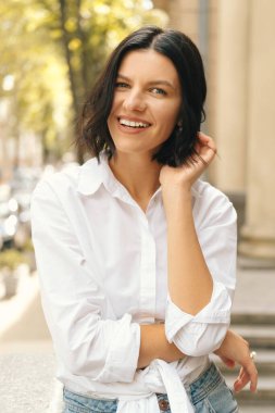 Şehrin arka planındaki kameraya bakan gülümseyen genç bir kadının dikey portresi..