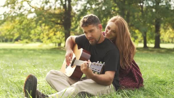 若いですロマンチックなカップル座って屋外で日没で自然と男遊びでアコースティックギター — ストック動画