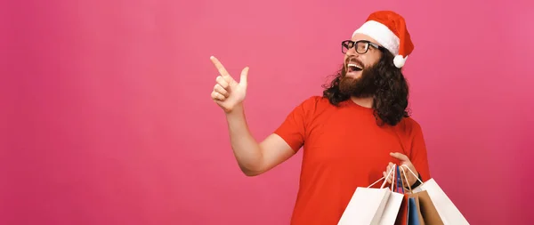 ピンクのパノラマの男でクリスマスの帽子を指し脇にコピースペースと保持紙袋 — ストック写真