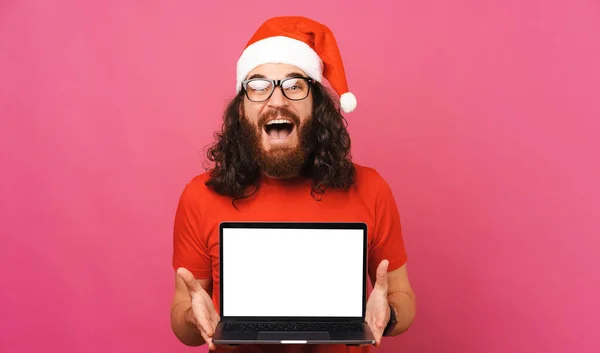 驚きの男はクリスマスの提供のための空白の画面と開いているラップトップを保持しています ピンクを背景にしたスタジオ写真 — ストック写真