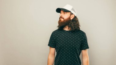 Ciddi kıvırcık sakallı bir adamın portresi. Stüdyoda, açık gri arka planda süpermen gibi yan yan bakıyor..