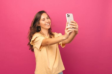 Ameze edilmiş genç bir kadının pembe arka planda akıllı telefonuyla selfie çektiği fotoğraf..