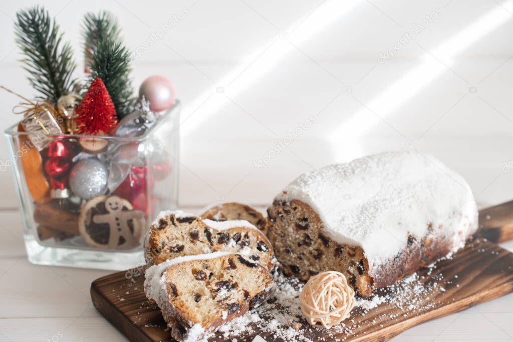 Traditional Christmas stollen made of dried fruits and nuts sprinkled with powdered sugar on the background of a Christmas decor with candles. Traditional Christmas cupcake.