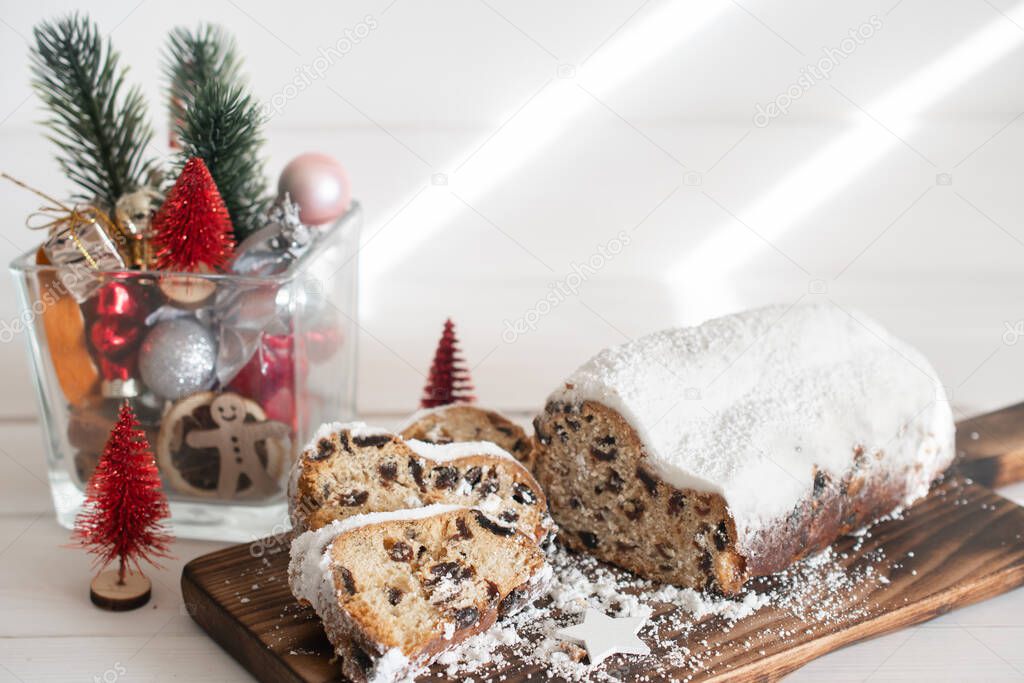 Traditional Christmas stollen made of dried fruits and nuts sprinkled with powdered sugar on the background of a Christmas decor with candles. Traditional Christmas cupcake.