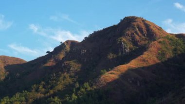 Mavi gökyüzüne karşı yamaçlarında ağaçlar olan eski büyük dağlar, Zaman Geçidi.