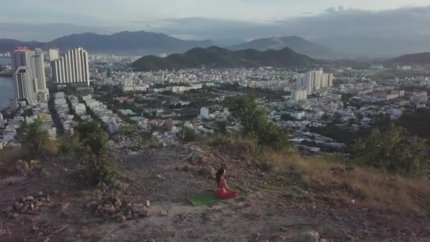 Kobieta uprawia jogę w Lotus pozować przeciwko miastu w pobliżu gór — Wideo stockowe