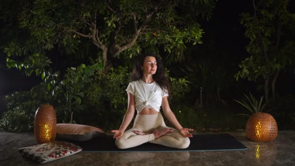 Mujer disfruta del yoga en posición Lotus en alfombra negra por la noche — Vídeo de stock